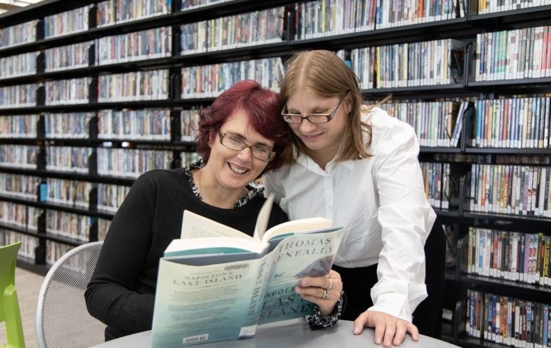 two women reading a book in library